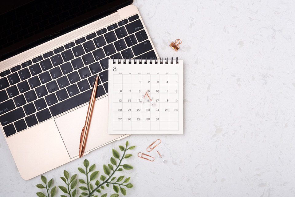 a calender with a rose gold pen sitting upon a laptop