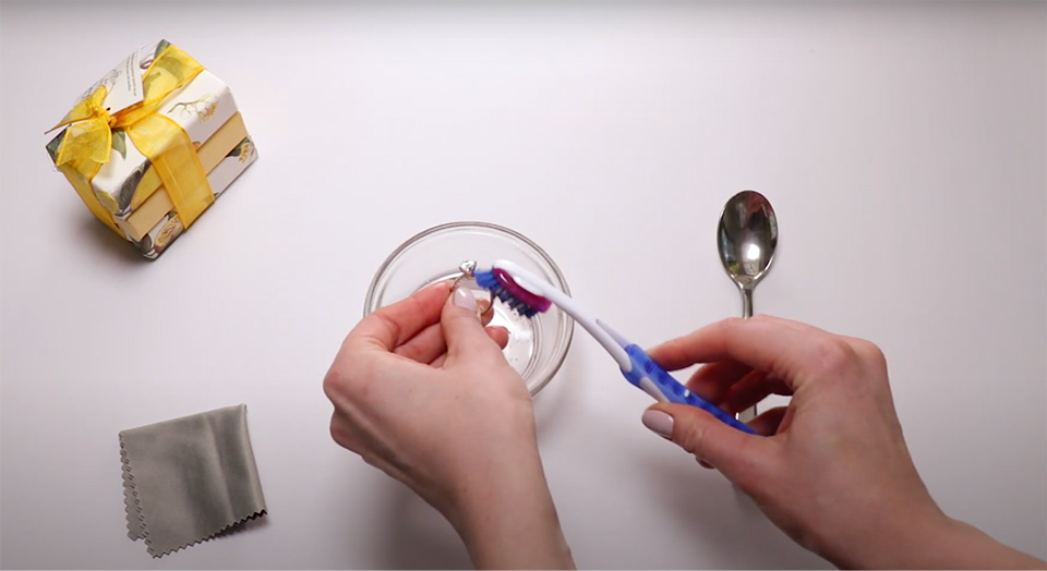 a woman gently scrubbing an engagement ring with a toothbrush