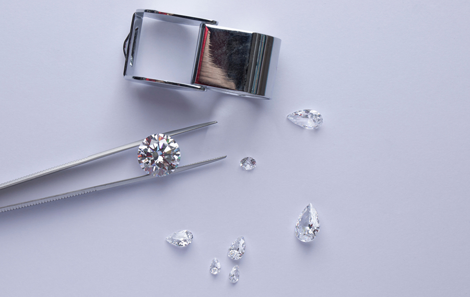 an array of diamonds with a pair of tweezers and a jewelers glass