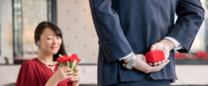 a man with a ring behind his back standing in front of a woman holding a bouquet of flowers