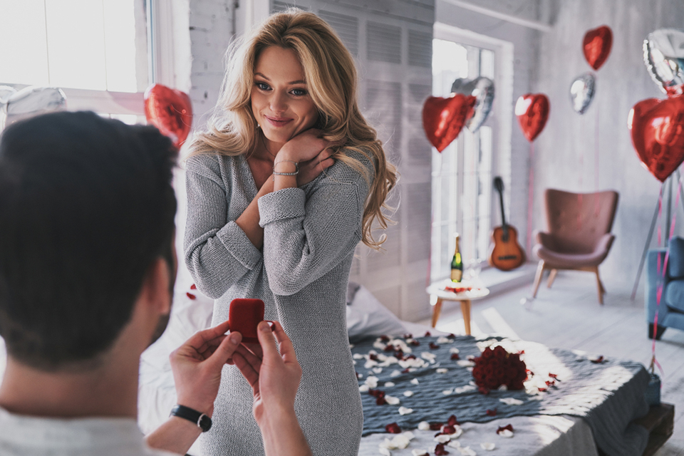 a man proposing to a woman with red heart balloons in the background